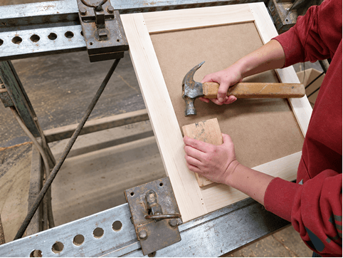 Craftsman assembling a cabinet door frame with a hammer and tapping block in the workshop